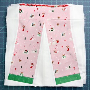May include: A pink fabric panel with a white centre and green trim. The fabric has a repeating pattern of mice, Christmas trees, and stars. The panel is sewn together with white fabric.