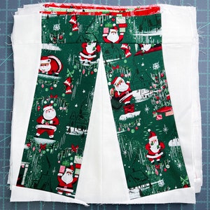 May include: Two strips of green fabric with a white background and a repeating pattern of Father Christmas figures, Christmas trees, and baubles. The fabric is sewn together to create a V-shape.