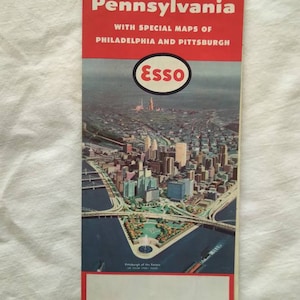 Könnte beinhalten: Vintage Pennsylvania Reisekarte mit Spezialkarten von Philadelphia und Pittsburgh. Das Cover ist rot mit weißem Text und einem Esso-Logo. Die Karte zeigt eine detaillierte Illustration einer Stadt mit Brücken und Gebäuden.