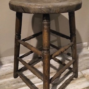May include: A wooden stool with a round seat and a ladder-like design on the legs. The stool is made of dark brown wood and has a rustic appearance.