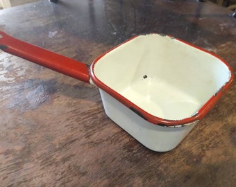 May include: White enamel saucepan with a red handle. The saucepan has a square shape and a slightly chipped rim.