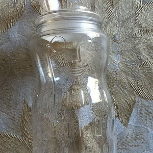 May include: A clear glass jar with a wide mouth and a textured surface. The jar has a lid with a pour spout.