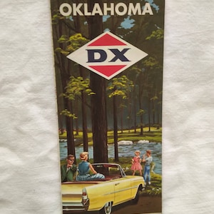 May include: Vintage Oklahoma travel brochure featuring a scenic illustration of a forest and river with a yellow convertible car. The brochure has the text "OKLAHOMA" at the top and "See America BEST... by car!" at the bottom.