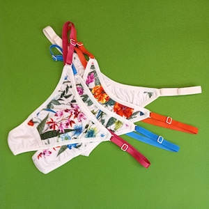 May include: Three pairs of white floral print underwear with adjustable straps. The straps are in red, blue and orange.