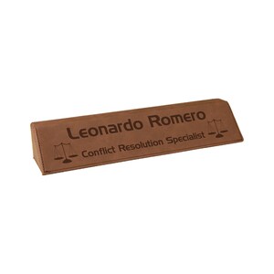 May include: A brown desk nameplate with the name "Leonardo Romero" and the title "Conflict Resolution Specialist" engraved on it. The nameplate also features a scales of justice symbol.
