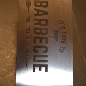 May include: A rectangular stainless steel barbecue spatula featuring the engraved text BARBECUE, IT'S TIME TO, FOOD, FRIENDS AND FUN, and the name GARY. The design includes a small spatula icon, a fork icon, and a cow silhouette in black lettering.