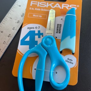 May include: Blue Fiskars kids' scissors, 12.7 cm long, with blunt tips, on an orange card. The package includes a blue eraser sheath. The scissors are designed for children aged 4-7 years old.