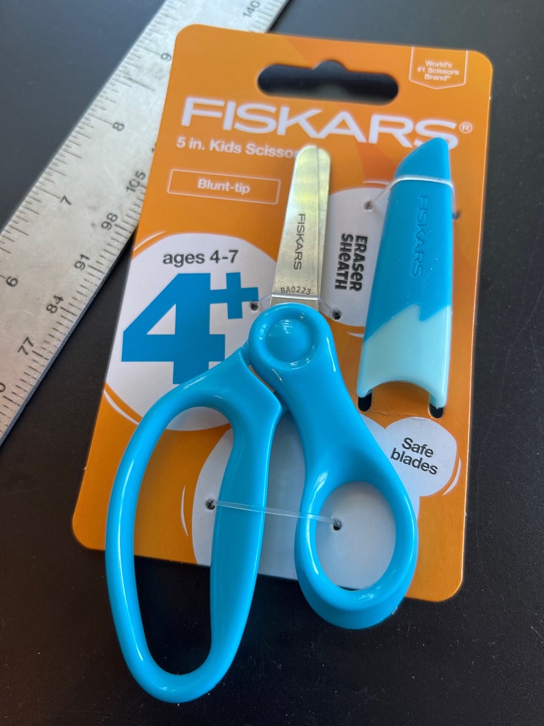 May include: Blue Fiskars kids' scissors, 12.7 cm long, with blunt tips, on an orange card. The package includes a blue eraser sheath. The scissors are designed for children aged 4-7 years old.