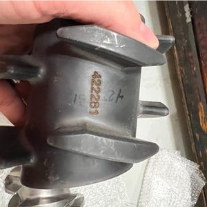 May include: A dark gray metal component with a series of blades and the number "422281" printed on the side. The component has a complex shape with multiple protrusions and a textured surface. The item is held by a hand.