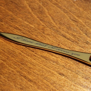 K&ouml;nnte beinhalten: Ein goldfarbener Brief&ouml;ffner mit Holzgriff. Die Klinge tr&auml;gt die Inschrift "I knew that I loved you" in Schreibschrift. Der Griff ist dunkelrot mit goldenen Akzenten.