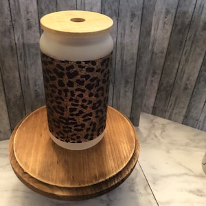 May include: A white ceramic jar with a wooden lid and a leopard print design. The jar is sitting on a wooden stand.