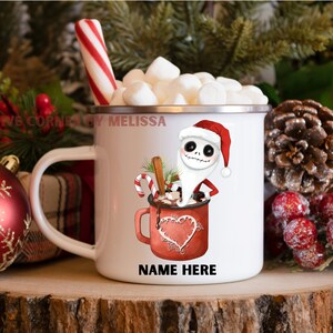 May include: White enamel mug with a red and white candy cane, marshmallows, and a cartoon character dressed as Santa Claus holding a mug of hot chocolate. The mug has the text "NAME HERE" on the bottom.