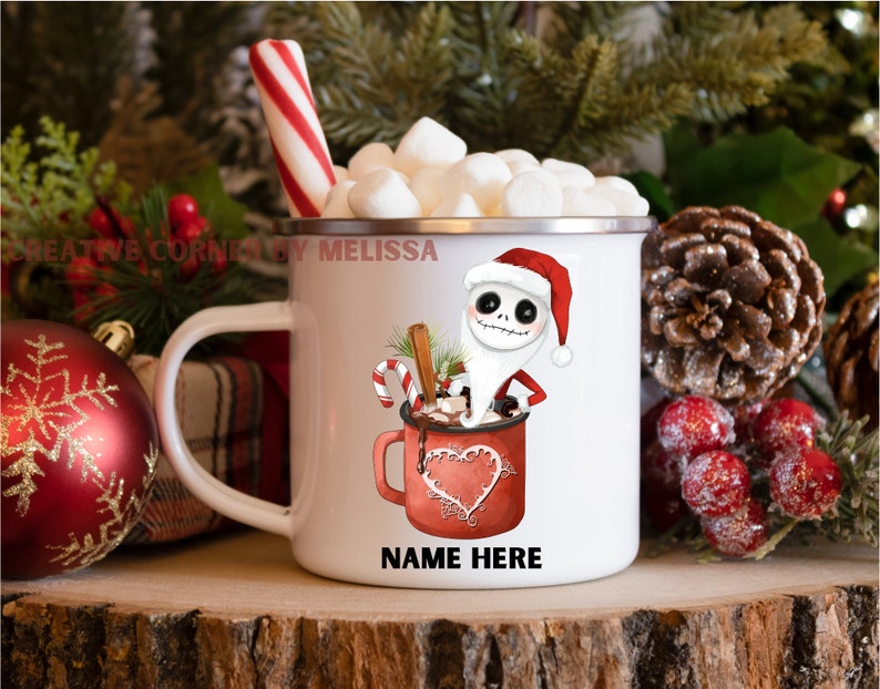 May include: White enamel mug with a red and white candy cane, marshmallows, and a cartoon character dressed as Santa Claus holding a mug of hot chocolate. The mug has the text "NAME HERE" on the bottom.