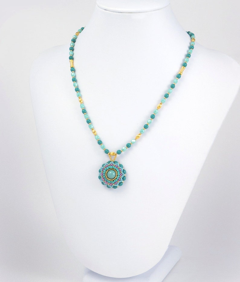 May include: A turquoise and gold beaded necklace with a turquoise and pink beaded pendant. The pendant is a circular design with a turquoise stone in the center.