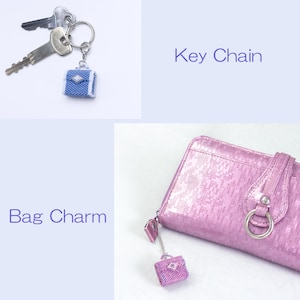 May include: A blue beaded purse charm with a silver ring attached to a silver key chain. The charm is also shown attached to a pink purse with a silver ring.