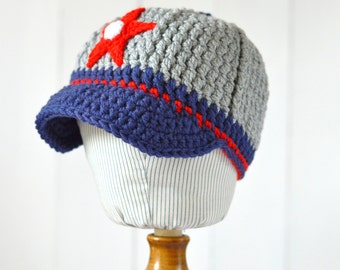 May include: A gray and blue crocheted baseball cap with a red star and white pom-pom on top.