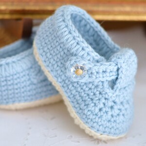 May include: A pair of light blue crocheted baby shoes with a white trim and a gold button detail.