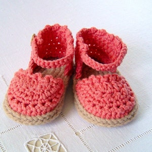 May include: A pair of crocheted baby sandals in a coral pink color with a brown sole.