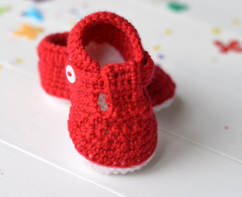 May include: A pair of red crocheted baby booties with white trim and a white button on the strap.