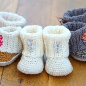 May include: Four pairs of crocheted baby booties in white and gray with different embroidered designs. The booties have a fold-over cuff and a textured sole.