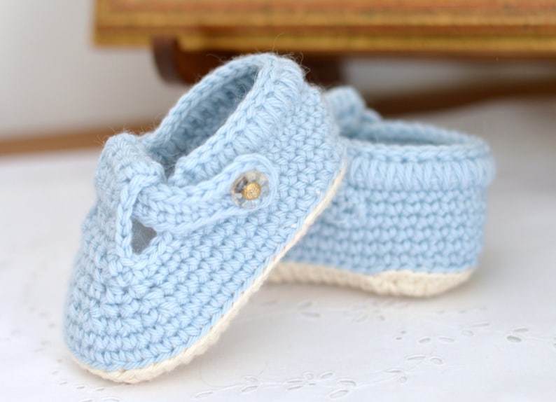 May include: A pair of light blue crocheted baby booties with a white trim and a button detail.