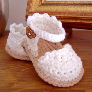 May include: White crocheted baby shoes with a brown button and a tan sole.