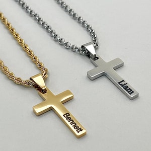 May include: Two gold and silver necklaces with cross pendants. The gold cross has the name "Bennett" engraved on it, and the silver cross has the name "Liam" engraved on it.
