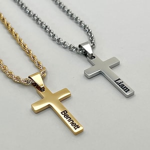 May include: Two cross pendants on chains. One gold-tone rope chain with a cross engraved with the name Bennett, and one silver-tone ball chain with a cross engraved with the name Liam. Both pendants feature a smooth, polished metallic finish.