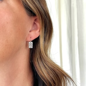 May include: Silver dangle earrings with a textured rectangular design.