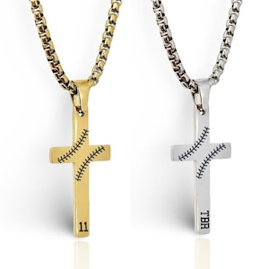 May include: Two cross necklaces with baseball stitching detail. One is gold-toned with the number 11, the other is silver-toned with "TBR". Both hang from a chain.