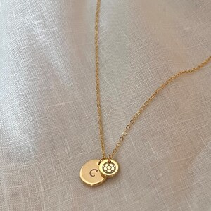 May include: A gold chain necklace with two charms. One charm is a round disc with the letter "C" engraved on it. The other charm is a round disc with a soccer ball design.
