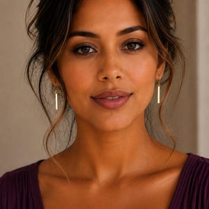 May include: A pair of gold-toned drop earrings featuring a slender, vertical rectangular bar design. The earrings hang from simple wire hooks, showcasing a polished metallic finish that catches the light, creating a clean and understated appearance.