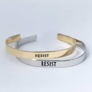 May include: Two gold and silver bracelets with the word "RESIST" engraved on them.