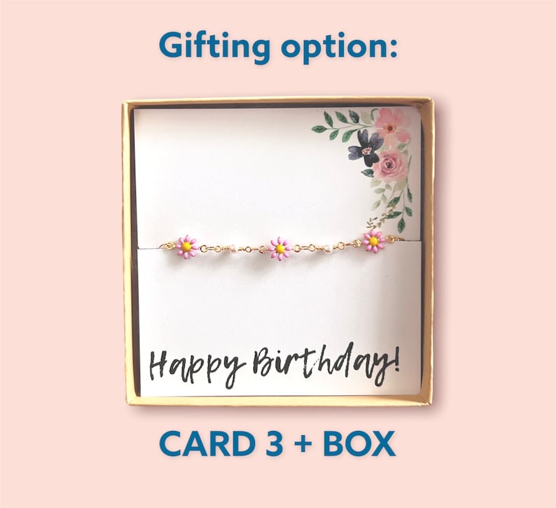 May include: A gold chain bracelet with pink daisy charms, presented in a gift box. The card inside reads "Happy Birthday!" with floral accents. The box is gold-coloured and the text "CARD 3 + BOX" is at the bottom.