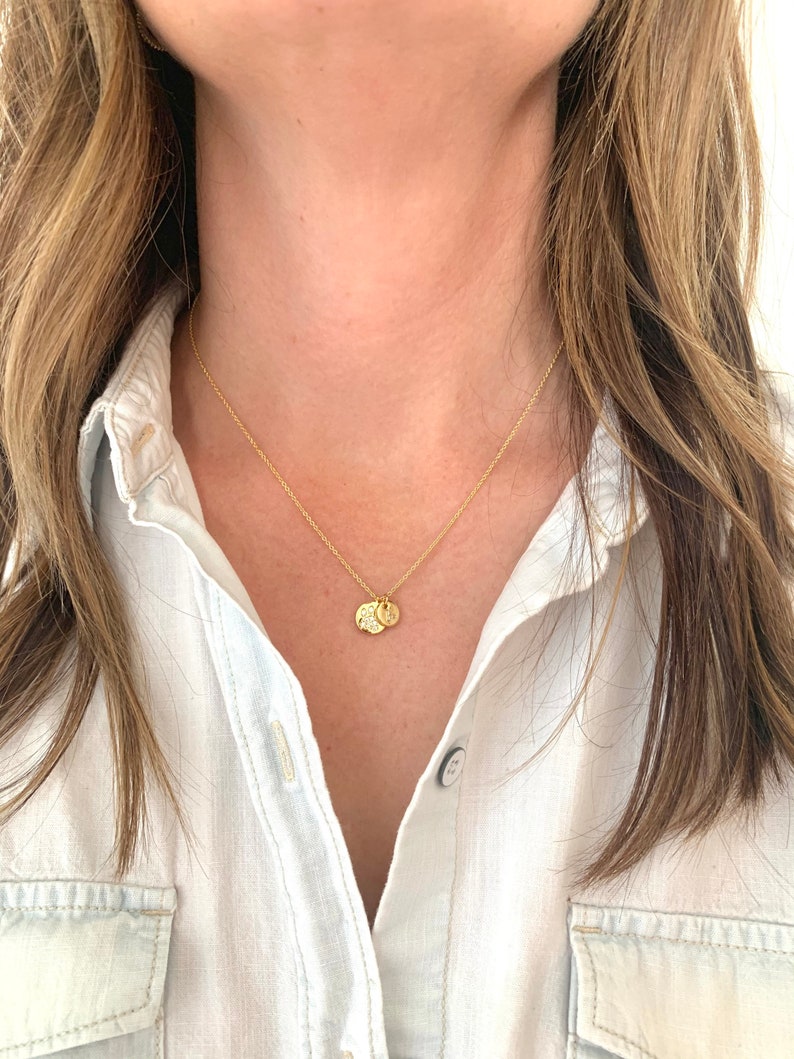 May include: A gold chain necklace with two small, round pendants. The pendants are engraved with letters.