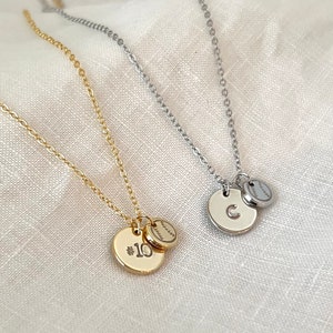 May include: Two gold and silver necklaces with baseball charms. One necklace has a charm with the number 10 and the other has a charm with the letter C.