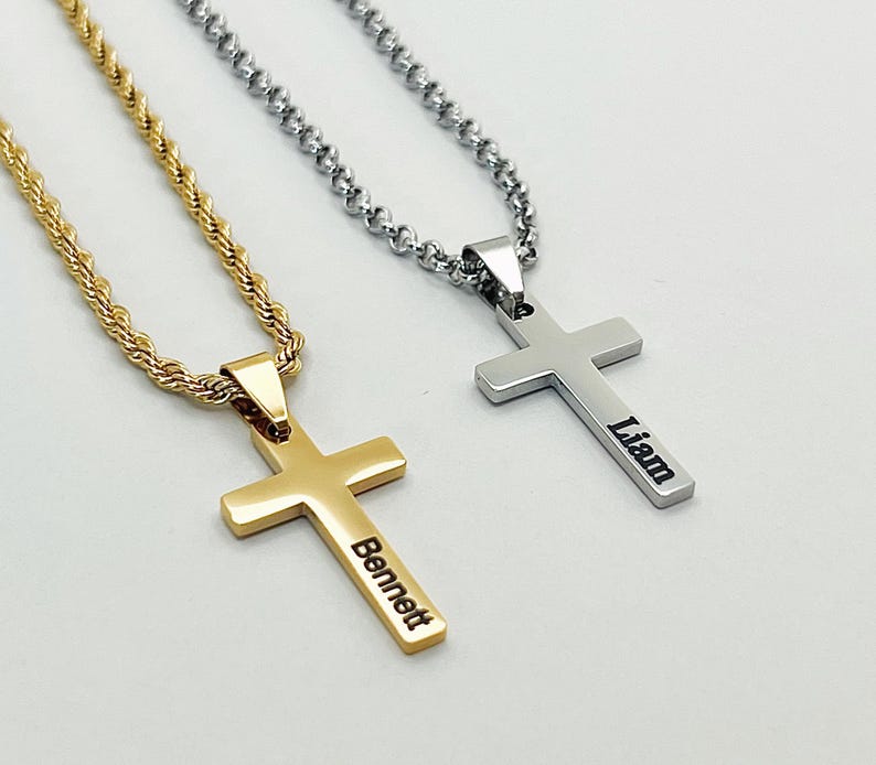May include: Two cross necklaces. One is gold-colored with the name "Bennett" engraved on it. The other is silver-colored with the name "Liam" engraved. Both necklaces have a rope chain.