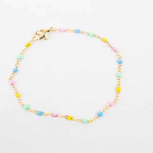 May include: A gold-coloured bracelet with a chain and small, pastel-coloured beads. The bracelet has a lobster clasp. The beads are in pink, yellow, blue, and green.