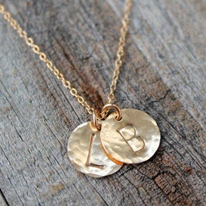 May include: Gold necklace with two hammered disc pendants, one with the letter 'L' and the other with the letter 'B'.