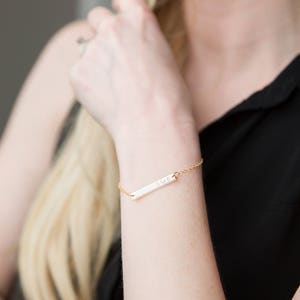 May include: A gold bar bracelet with a delicate chain and a personalized inscription that reads "DVR".