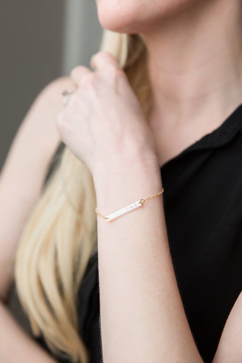 May include: A gold bar bracelet with a delicate chain and a personalized inscription that reads "DVR".
