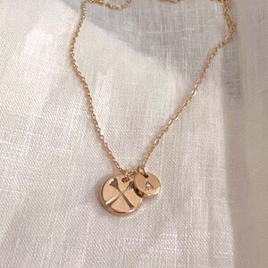 May include: A gold chain necklace with two charms. One charm is a round disc with a cross design, and the other charm is a round disc with the letter "A" engraved on it.