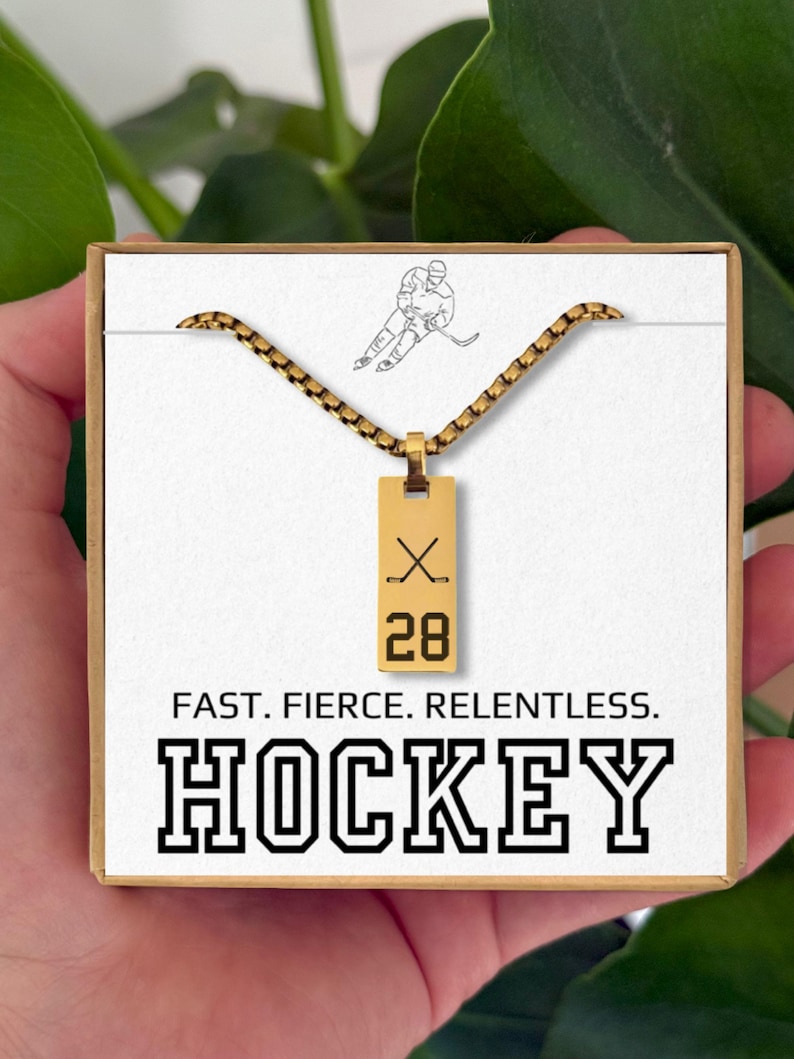 May include: Gold-colored hockey necklace with a rectangular pendant featuring crossed hockey sticks and the number 28. The card reads "FAST. FIERCE. RELENTLESS. HOCKEY."