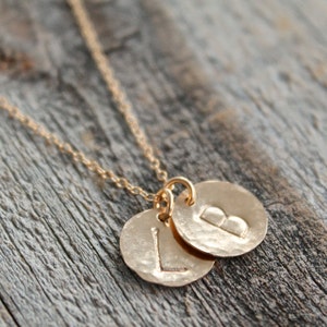 Puede incluir: Collar de oro con dos colgantes redondos, uno con la letra "L" y el otro con la letra "B".
