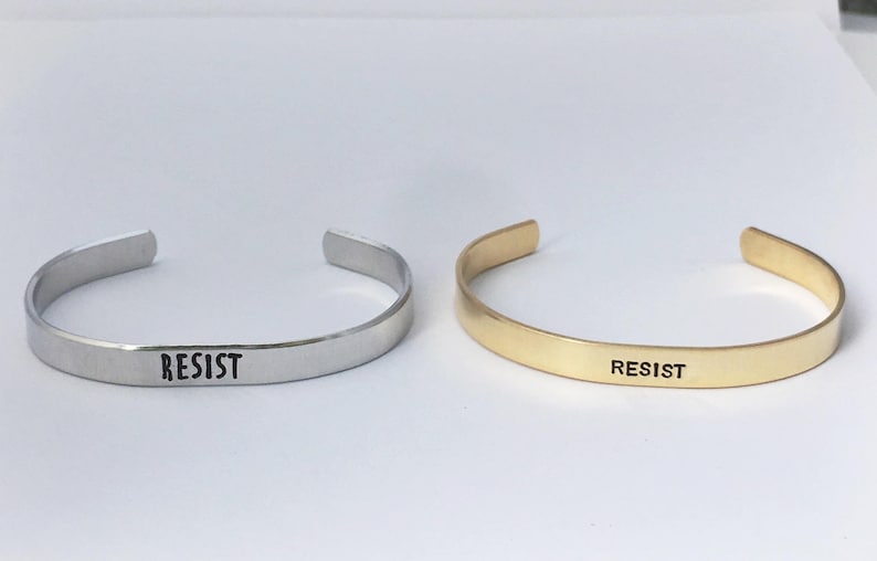 May include: Two simple silver and gold bracelets with the word "RESIST" engraved on them.