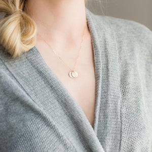 Puede incluir: Un delicado collar de oro con dos peque&ntilde;os colgantes redondos. El collar lo lleva una persona que lleva un su&eacute;ter gris.