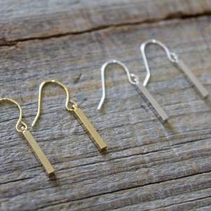 May include: Two pairs of drop earrings featuring a vertical bar design. One pair is finished in a polished gold tone, while the other pair is finished in a polished silver tone. Each earring includes a curved ear wire hook for attachment.