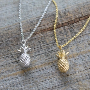 Può includere: Due collane a forma di ananas, una d'argento e una d'oro, su una superficie di legno.