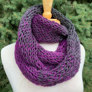 May include: A purple and gray infinity scarf knitted in a chunky yarn. The scarf is made with a gradient of purple and gray yarn.