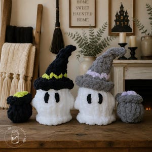 May include: Two white plush ghost figures wearing textured hats, one black with a lime green band and one gray with a light purple band, accompanied by two small matching plush cauldrons on a wooden surface.